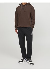 Hnědá mikina s kapucí s logem, přední kapsou a šňůrkou, v kombinaci s černými tepláky s bočním logem a elastickým pasem.