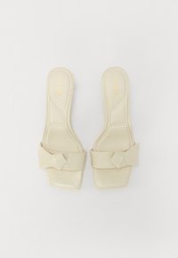 Beige slide sandals with a glossy finish, square toe, and a large bow detail on the strap. Logo printed on the insoles.