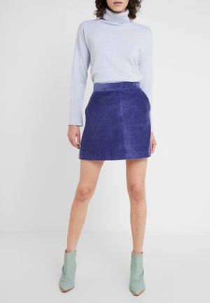 Jasnoniebieski sweter z golfem w połączeniu z fioletową mini spódnicą z sztruksu. Modelka nosi zielone botki za kostkę z zaostrzonymi noskami i niewielkim obcasem.