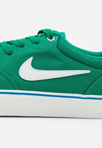 Green canvas sneakers with a white swoosh logo, blue accent stripe on the sole, and round laces. Smooth texture and low-profile design.