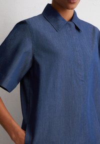 Donkerblauwe shirt van denim met een kraag, korte mouwen en een voorflap. Gladde textuur met zichtbare stikseldetails.