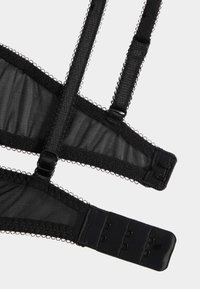 Zwarte mesh bralette met een textuurontwerp, verstelbare bandjes, haak-en-oogsluiting en delicate geschulpte rand langs de randen.