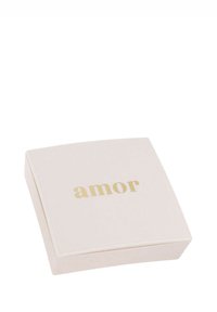 Piccolo cofanetto quadrato beige per gioielli con la scritta dorata "amor" sul coperchio, su uno sfondo bianco.