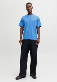 Sinine puuvillane T-särk lühikeste varrukatega ja ümar kaelus, koos tumedate denimitest laiade pükstega, millel on kontrastõmblused ja massiivsed kingad.