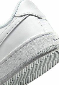 Sneaker de cuero blanco con suela texturizada, parte superior lisa y suela de goma con un patrón en forma de chevrón. Branding sutil en el lateral.