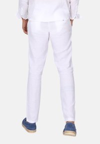 Bílé lněné kalhoty s rovný střih, které mají hladkou texturu a nedokončený lem. Kombinované s modrými botami, což ukazuje na ležérní styl.