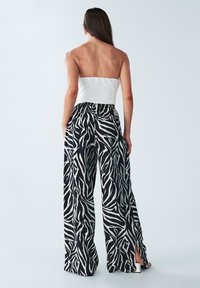 Strapless witte top met zwart-witte zebraprint wijde broek met zijsplitten. Lichtgewicht stof met een losse pasvorm.