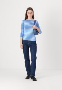 Blauw-wit gestreepte lange mouwen top met een ronde hals, gecombineerd met donkerblauwe rechte jeans en zwarte schoenen. Houdt een kleine blauwe tas vast.