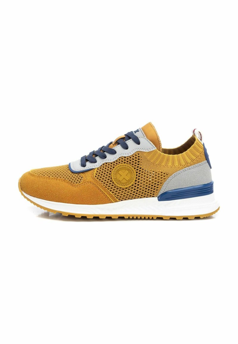 Zapatilla de malla amarilla con acentos grises y azules, paneles de ante texturizado, logo redondo y suela blanca. Diseño de cordones con cuello acolchado.