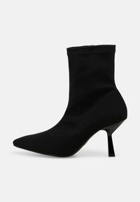 Stivaletto nero con punta a punta affilata, tacco a stiletto sottile di altezza media e chiusura con cerniera su sfondo neutro.