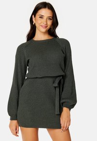 Abito a maglia a coste di colore verde scuro, con maniche lunghe a palloncino, vita cintrata con fascia da annodare e gonna attillata. Tessuto testurizzato.