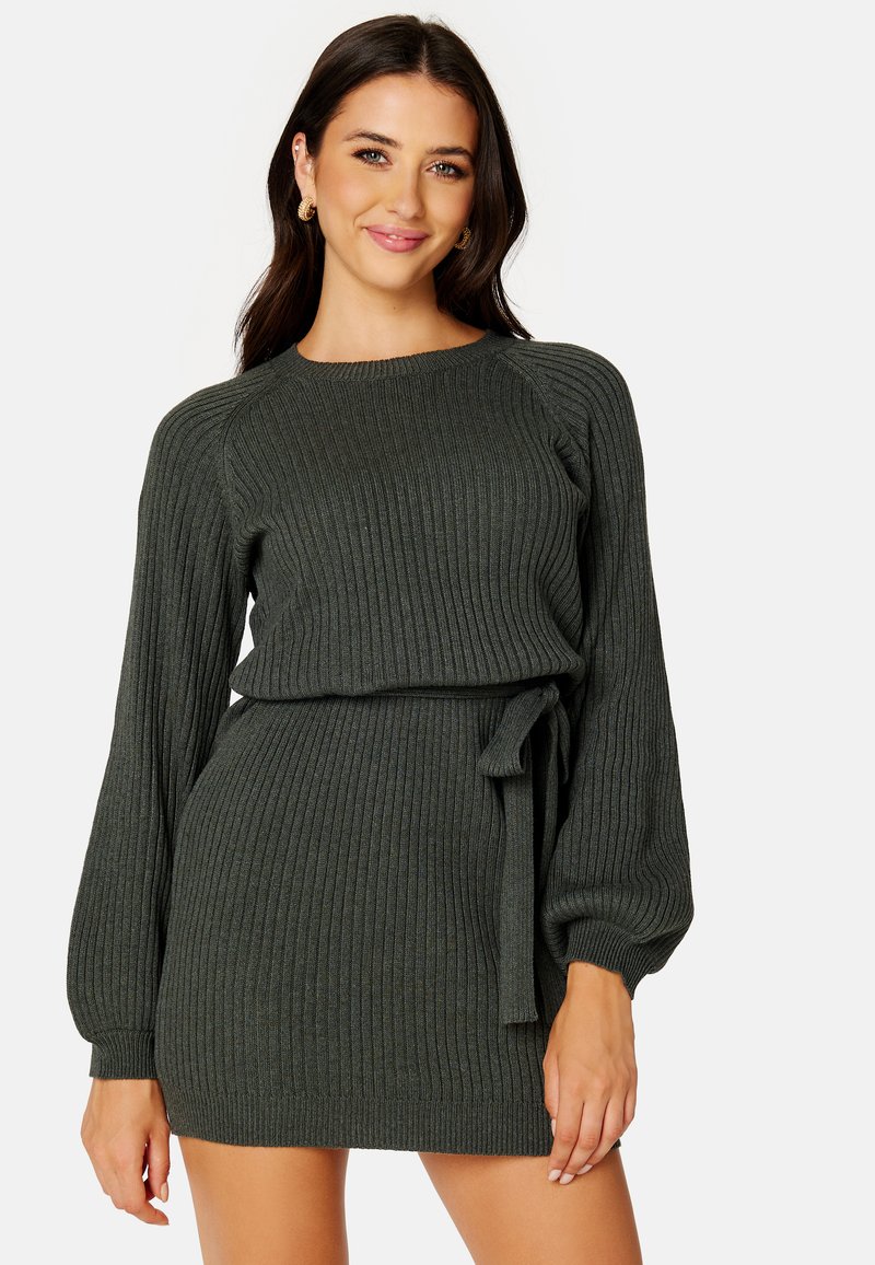 Abito a maglia a coste di colore verde scuro, con maniche lunghe a palloncino, vita cintrata con fascia da annodare e gonna attillata. Tessuto testurizzato.