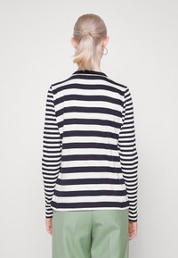 Maglietta a maniche lunghe caratterizzata da righe orizzontali blu navy e bianche, scollo rotondo e una texture in cotone morbido, abbinata a pantaloni verdi.
