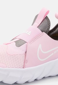 Chaussure de sport rose avec un dessus en maille, accents gris, logo blanc, bande extensible sur le cou-de-pied et semelle blanche texturée.