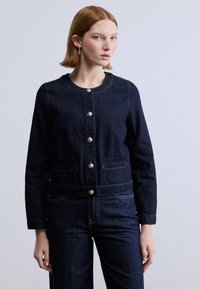 Σκούρο τζιν μπουφάν με στρογγυλή λαιμόκοψη, ασημί κουμπιά, δύο μπροστινές τσέπες και ελάχιστες ραφές. Συνδυασμένο με τζιν παντελόνι στο ίδιο χρώμα.