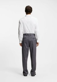 Graue Textilhose mit geradem Schnitt, flacher Vorderseite, Gürtelschlaufen und zwei Gesäßtaschen; getragen mit einem weißen Hemd.