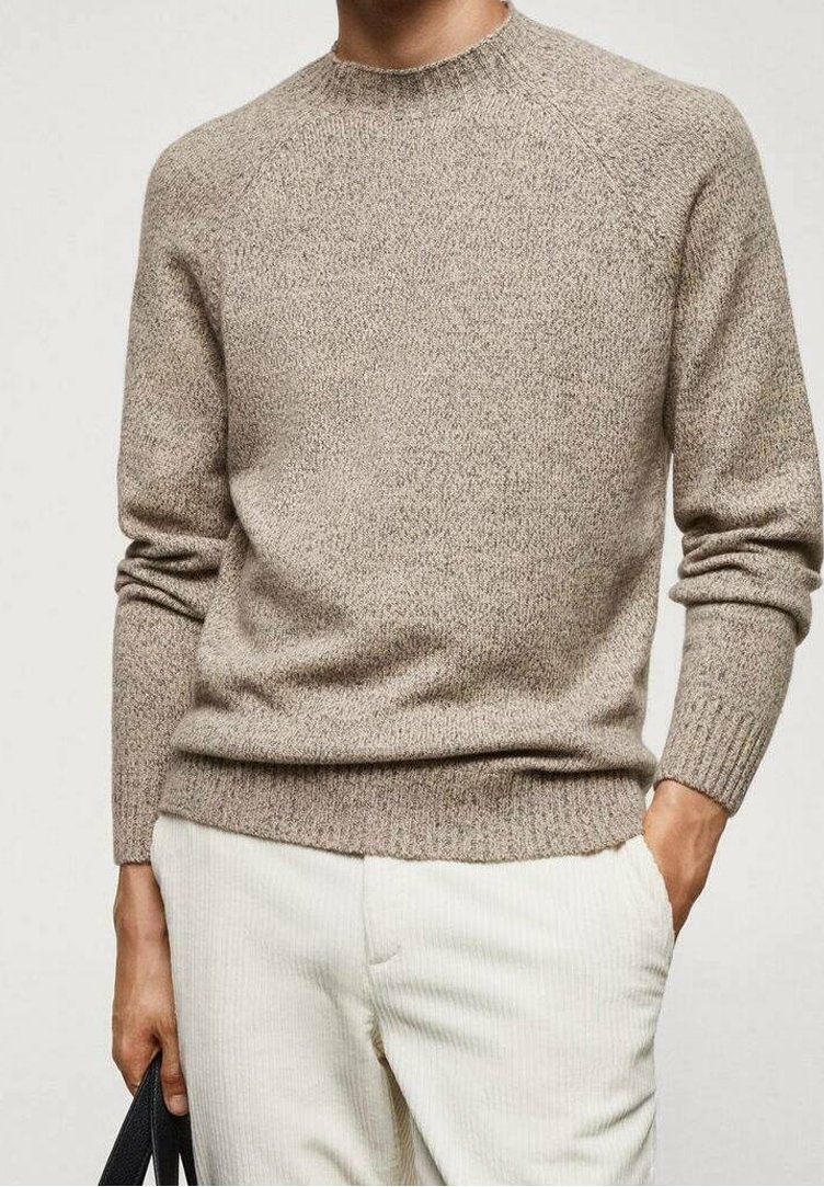 Homme portant un pull beige en tricot et un pantalon en velours côtelé blanc, tenant un sac noir dans la main gauche, main droite dans la poche.