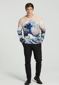 Sudadera de manga larga con un diseño de ola en azul y blanco, con una sección superior en rosa pálido; llevada con pantalones y zapatos negros.