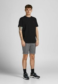 T-shirt en coton noir à manches courtes avec un petit logo rouge. Shorts gris à motif, retroussés à l'ourlet. Baskets noires avec des accents colorés.