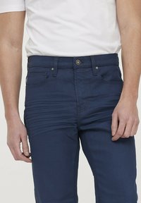 Marineblauwe broek van een katoenmix stof. Heeft een vijf-pocket ontwerp, voorknopsluiting en textuurdetails langs de dijen.