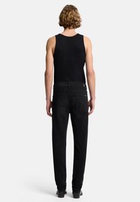 Schwarze Jeans aus Denim mit schmalem Schnitt, fünf Taschen und dezenten Markenlogos am Bund. Getragen mit einem schwarzen ärmellosen Oberteil.