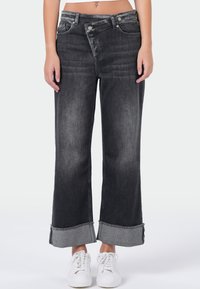 Zwarte denim wijde-pijpen jeans met een vervaagde afwerking, omgeslagen zoom, klassieke vijf zakken ontwerp en zilveren hardware. G gedragen met witte sneakers.