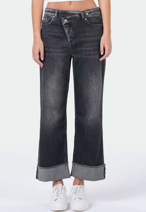 Zwarte denim wijde-pijpen jeans met een vervaagde afwerking, omgeslagen zoom, klassieke vijf zakken ontwerp en zilveren hardware. G gedragen met witte sneakers.