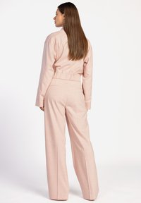 Lichtroze tweedelige outfit bestaande uit een cropped jack met elastische taille en lange mouwen, gecombineerd met hoge wijde broekspijpen.