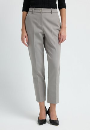 Woman wearing light gray tailored ankle-length trousers and black textured high-heeled shoes against a plain background.