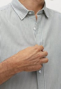 Szara i biała pasiasta koszula na guziki z kołnierzykiem, charakteryzująca się gładką teksturą i widocznymi detalami guzików, przedstawiona w momencie zapinania przez rękę.