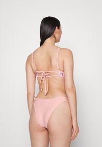 Biquíni rosa com faixa estampada de flores, alças ajustáveis e fecho com laço nas costas. Textura suave e cobertura mínima na parte de trás.