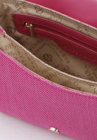 Pink taske med tekstureret stofydre, der har en glat læderindvendig og en lynlås lomme, præget med et gentaget logo mønster.