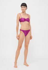 Lilla bikinitopp med rynker og tynne stropper, samt lavt båret underdel, laget av glatt, glinsende stoff.
