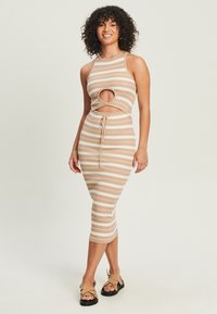 Béžové pruhované pletené šaty s vystrihnutým pásom a dĺžkou po strednú časť lýtok. V kombinácii s plochými sandálmi s remienkami.