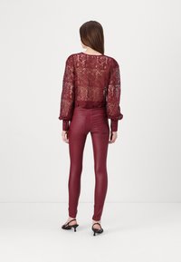 Mörkröd spetstopp med puffärmar och blommönster, ihop med högmidjade mörkröda leggings i konstläder. Svarta klacksandaler ingår.