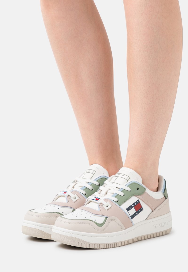 Baskets blanches et pastel avec une tige en cuir, présentant des accents verts et beiges, une boîte à orteils perforée, et un patch logo sur le côté.