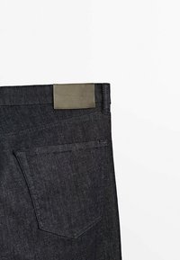 Mörk denimjeans med rak skärning, med en rektangulär grå etikett på midjebandet och en bakficka med format öppning.