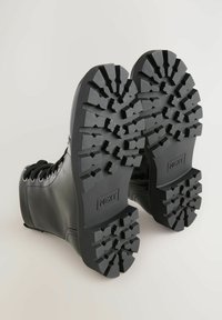 Stivali in pelle nera con suole in gomma texturizzata. Le suole presentano un motivo a zigzag per una migliore aderenza. Occhielli e lacci visibili.