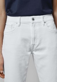 Vaqueros de denim blanco con corte recto, cuentan con un broche frontal, botón de metal y diseño de cinco bolsillos. Textura suave con un detalle mínimo.