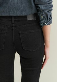 Černé džíny z denimu s přiléhavým střihem, dvěma zadními kapsami a texturovaným povrchem. Na pásku viditelná značka s logem.