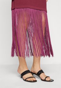 Βουργουνδής ριγέ τοπ με μακριά φούστα φούξια με φούντες, που αναδεικνύει ζωντανές κλωστές. Μαύρες πλεκτές παντόφλες ολοκληρώνουν την εμφάνιση.