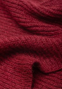 Czerwony, dziewiarski materiał o miękkiej, lekko teksturowanej powierzchni. Tkanina ukazuje mieszankę prążkowanych i gładkich obszarów.