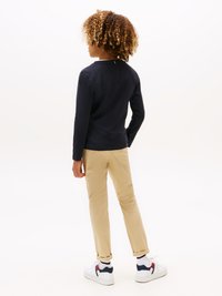 Navy long-sleeve shirt, beige pants, white sneakers with dark accents. Textured curls, view from behind, plain background.