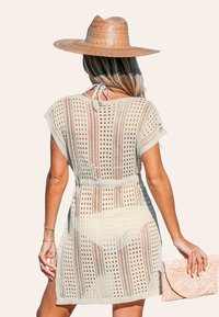 Strick-Überkleid in Beige mit offenem Netzdesign, kurzen Ärmeln und Kordelzug in der Taille. Accessoire: geflochtene Tasche in hellem Pfirsich.