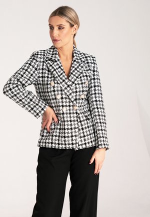 Dwurzędowa marynarka w czarno-białą kratę houndstooth z wyłogami, złotymi guzikami i długimi rękawami, zestawiona z czarnymi spodniami.