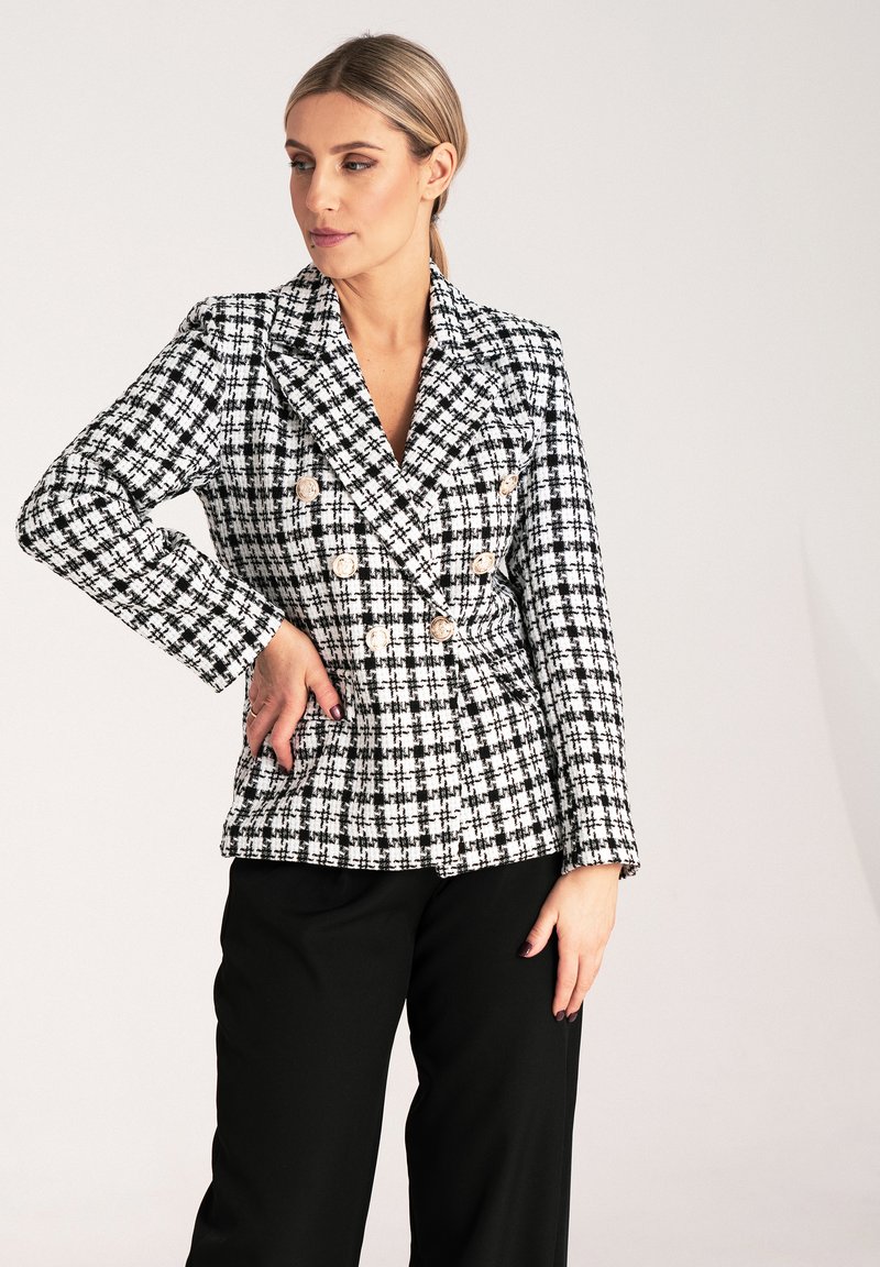 Dwurzędowa marynarka w czarno-białą kratę houndstooth z wyłogami, złotymi guzikami i długimi rękawami, zestawiona z czarnymi spodniami.