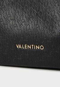Bolsa de mão em couro preto com padrão de texto em relevo e logótipo dourado "VALENTINO". Textura suave com uma forma estruturada.