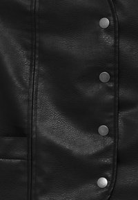 Veste en cuir synthétique noir présentant une surface texturée, des coutures visibles et cinq boutons-pression métalliques ronds sur la fermeture avant.