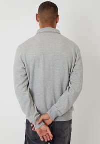 Szary sweatshirt z prążkowanym kołnierzem i mankietami, charakteryzujący się gładką teksturą i długimi rękawami. Tył prezentuje minimalistyczny design.