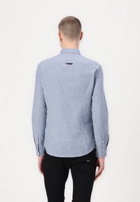 Camisa de manga larga azul claro con cuello puntiagudo, puños de botón y dobladillo recto. Textura sutil con un pequeño logo en la parte posterior.